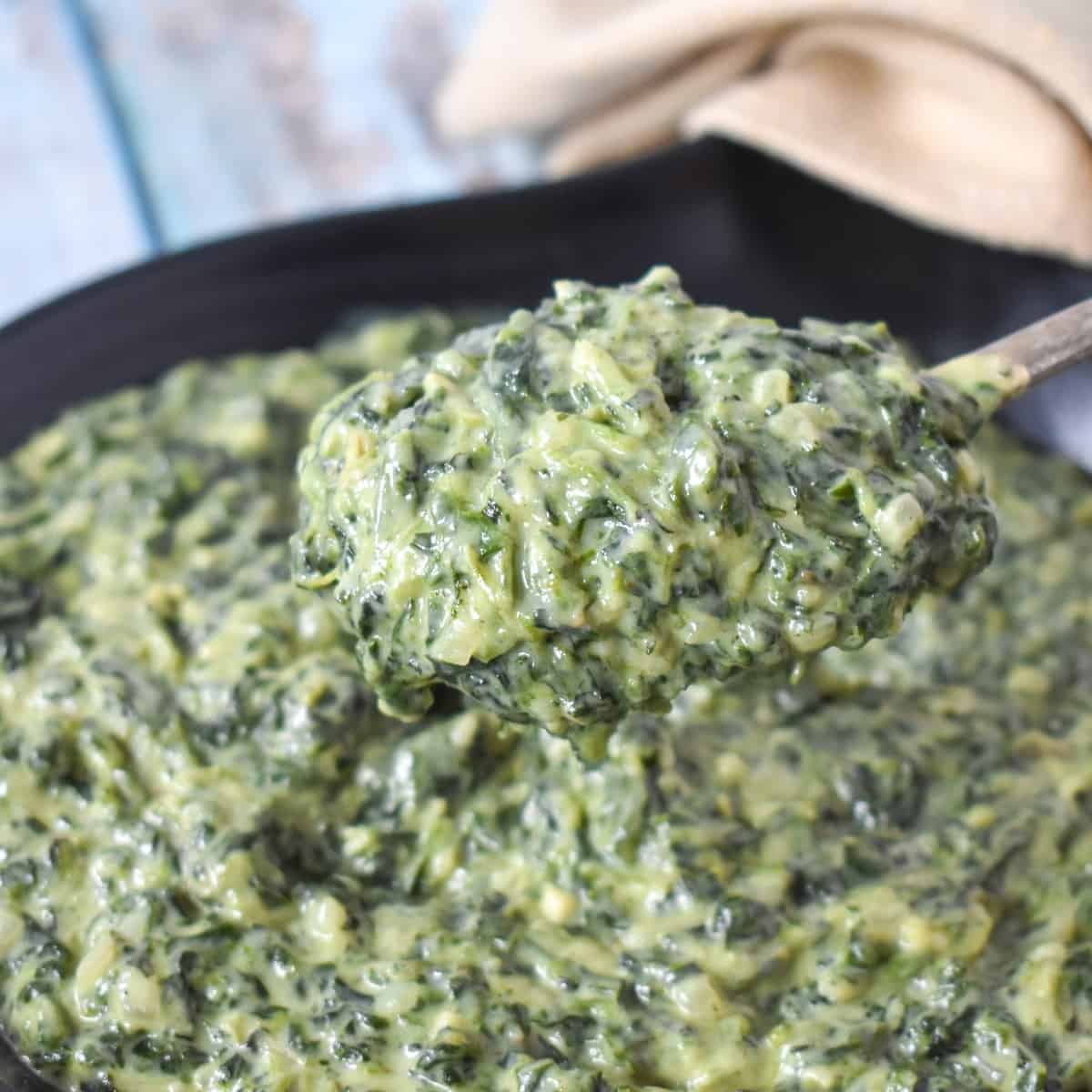 A close up of a spoonful of the creamed spinach that is served in a black dish.