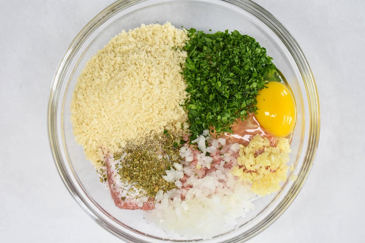 The ingredients for the meatballs in a glass bowl before mixing.