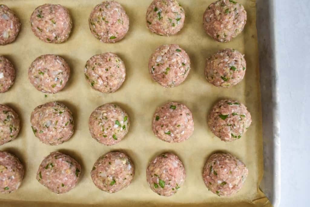 Formed turkey meatballs, before cooking, arranged on a parchment paper lined baking sheet.