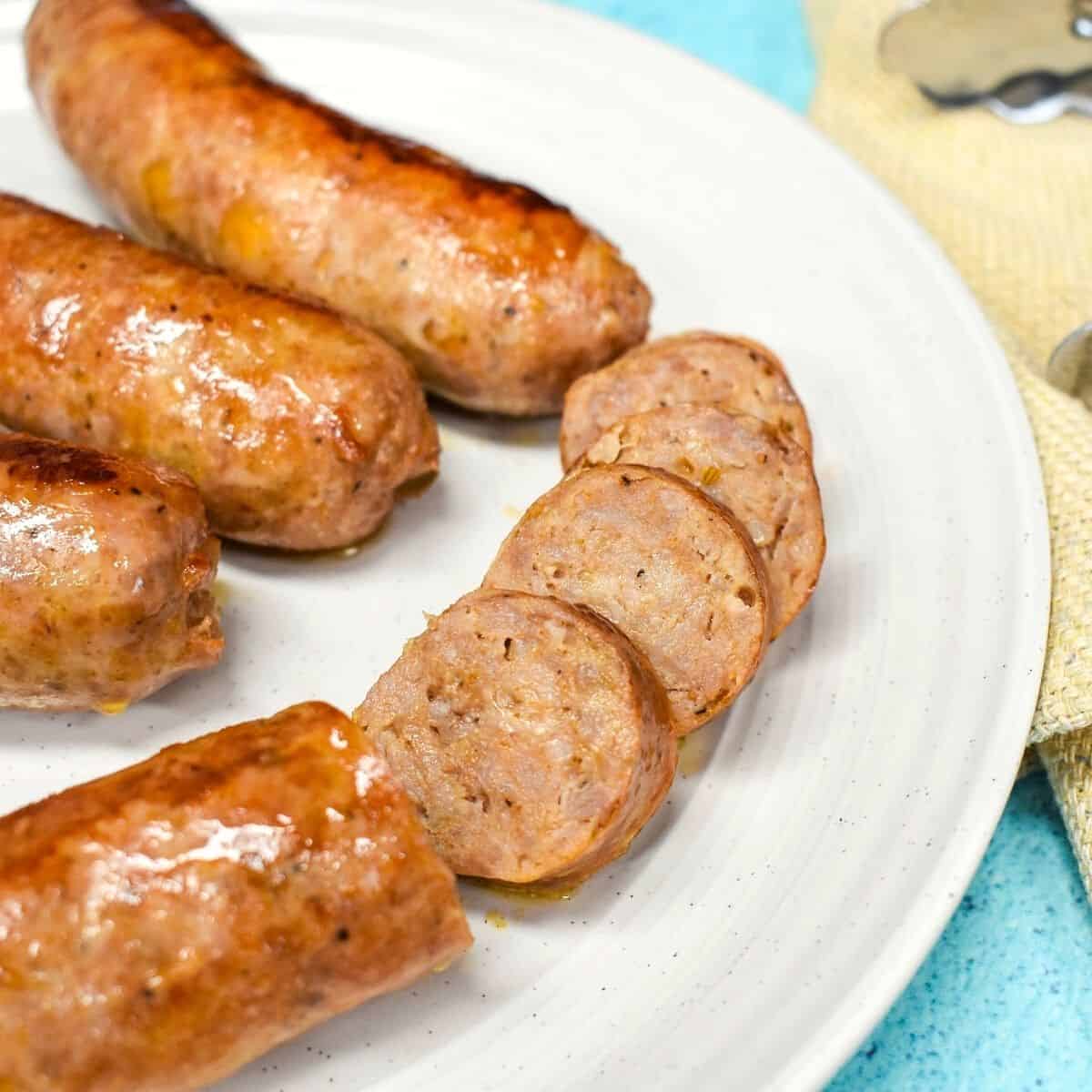 A close up image of the sausage served on a white plate. Part of one of the sausages is sliced into bite sized pieces.