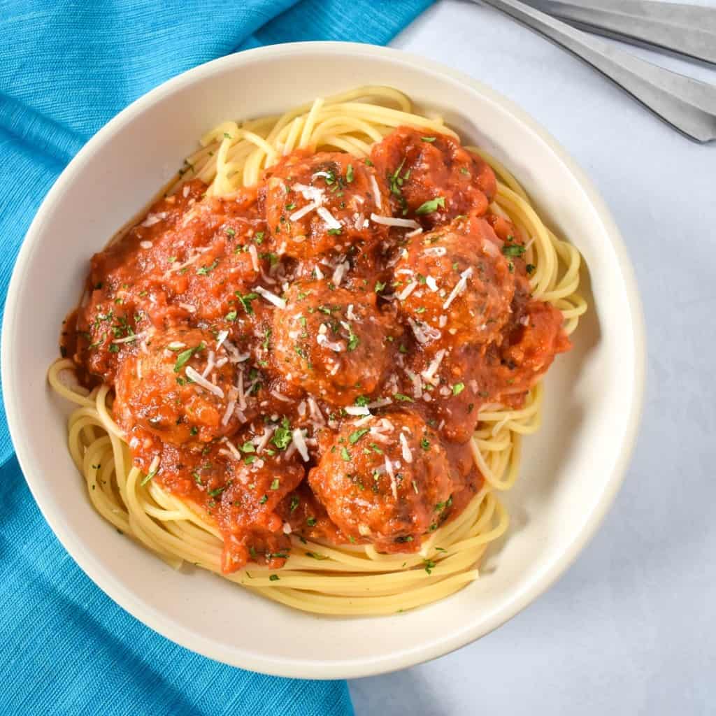 The spaghetti and turkey meatballs served in a white bowl, set on a white table with an aqua linen to the left side.