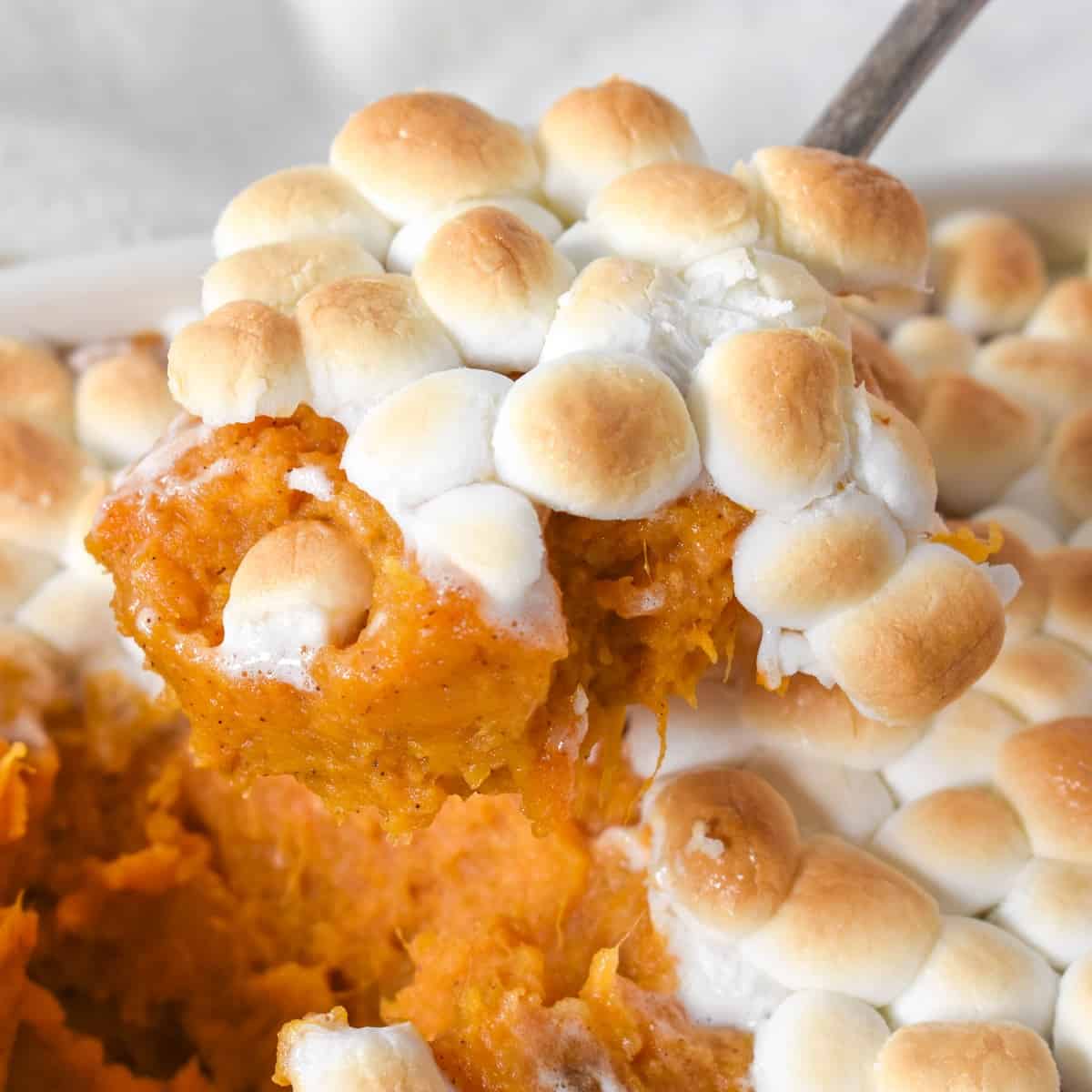 A spoonful of the sweet potatoes with marshmallows held up over the casserole.