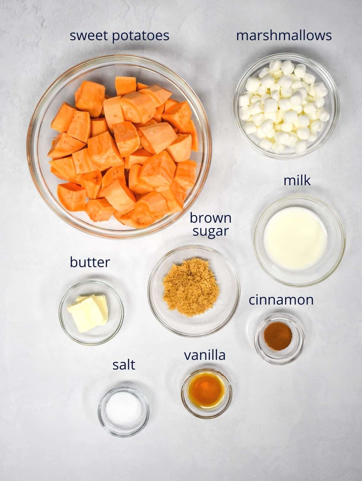 The ingredients for the dish prepped and arranged in glass bowls and set on a white table. Each ingredient has a small label with its name.