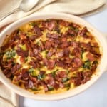 The baked brussels sprouts casserole served in an off-white dish with a beige linen on a white table.