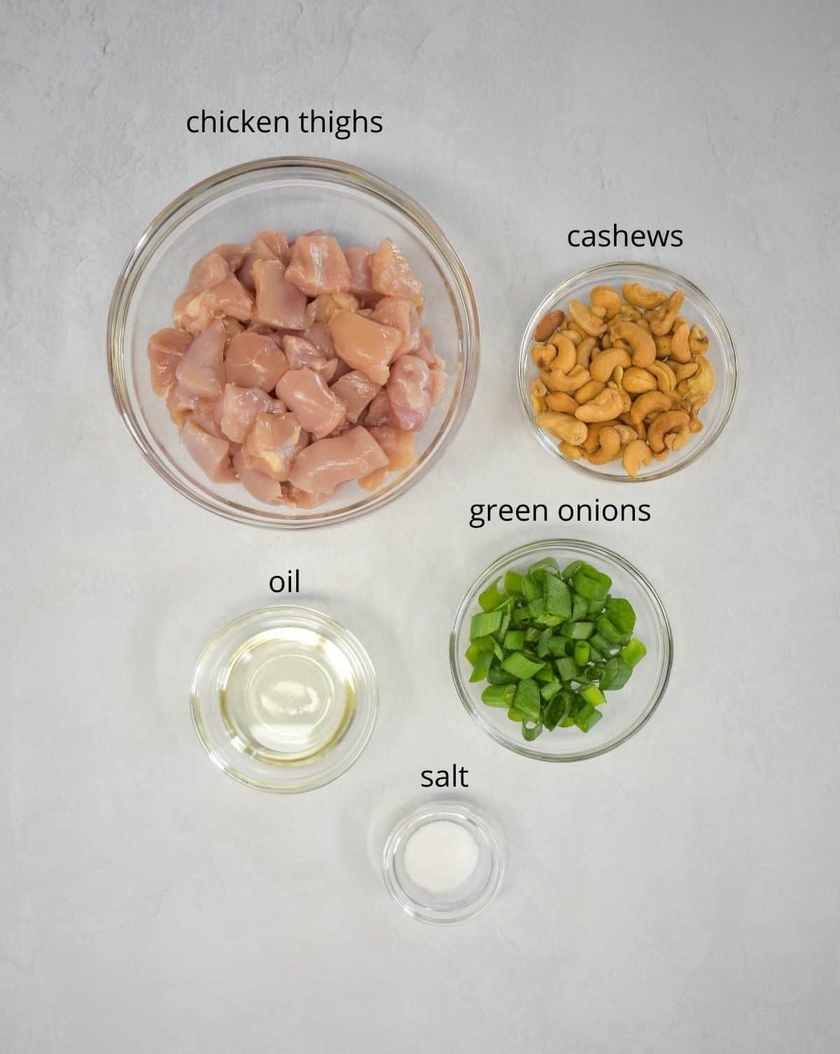 An image of the prepped ingredients to cook the chicken for the dish arranged in glass bowls and set on a white table.