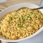 An image of the chicken flavored rice served in an oval white bowl with a spoon and a beige linen.