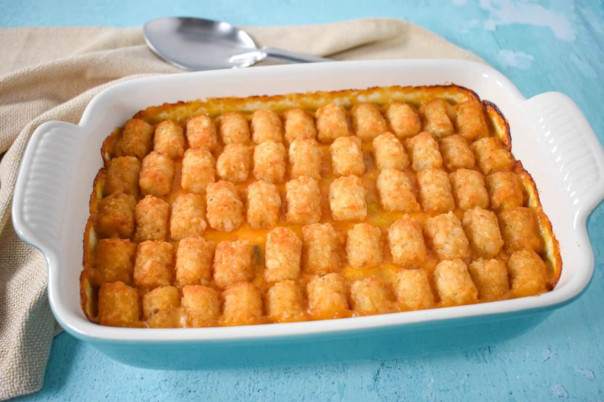 An image of the finished casserole in an aqua dish with a white interior. It is set on a light blue table with a beige linen and serving spoon.