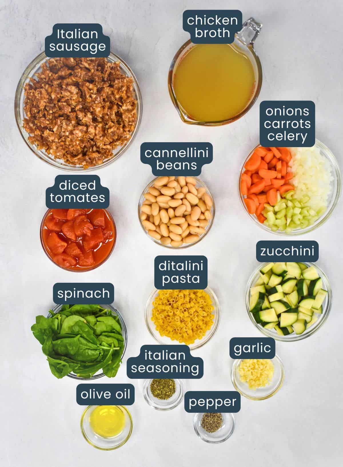 The ingredients for the soup prepped and arranged in glass bowls on a white table. Each ingredient is labeled.