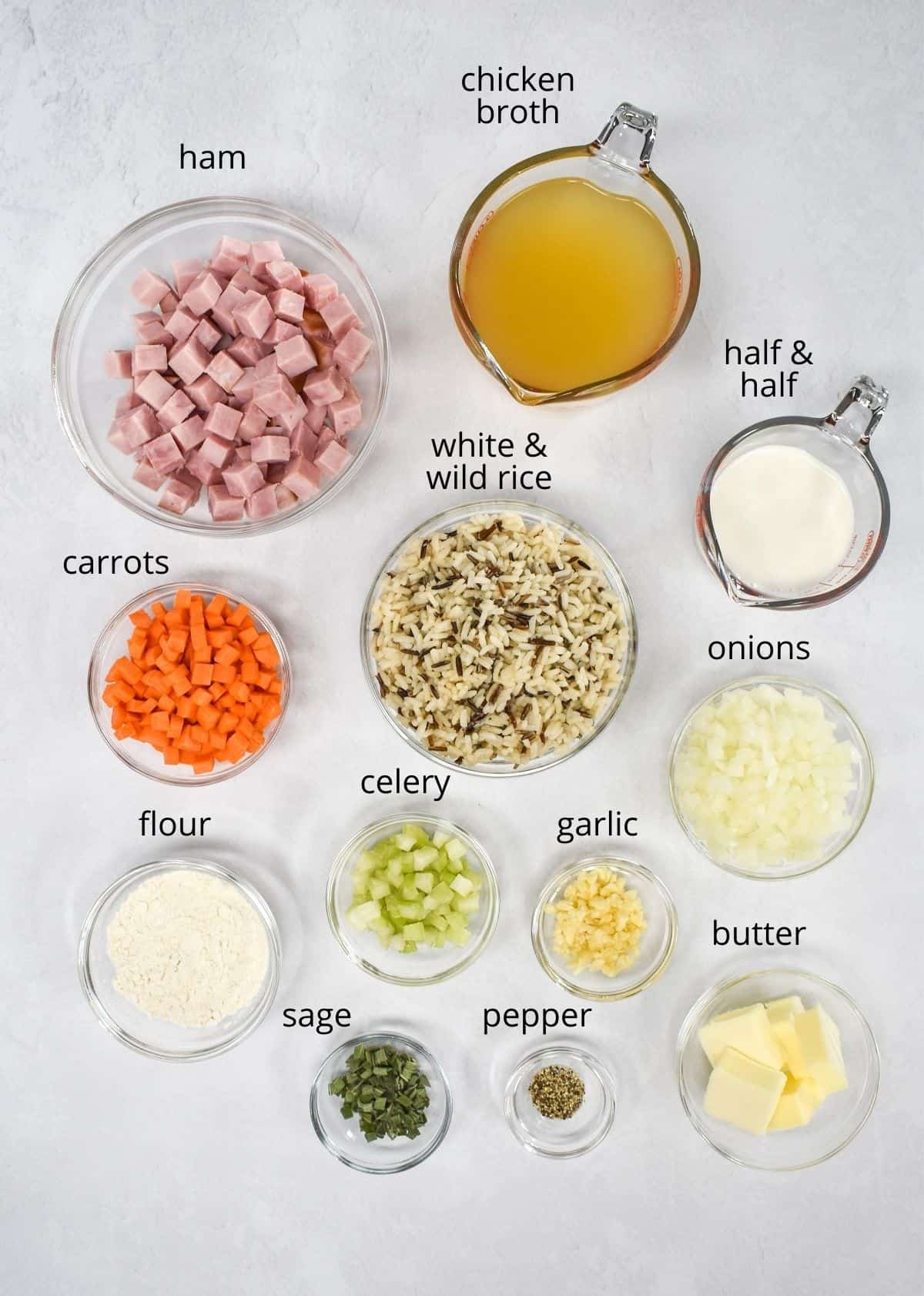 The ingredients for the soup prepped and arranged in glass bowls and set on a white table. Each ingredient has a label with the name above it in small black letters.