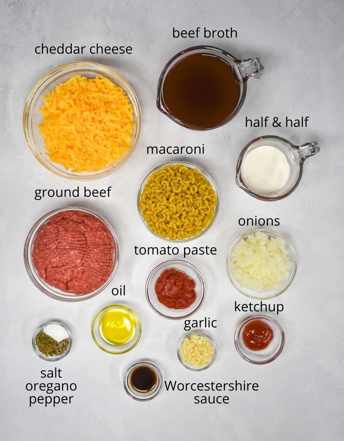 The ingredients for the dish prepped and arranged in glass bowls on a white table. Each ingredient has a label with the name above it in small black letters.