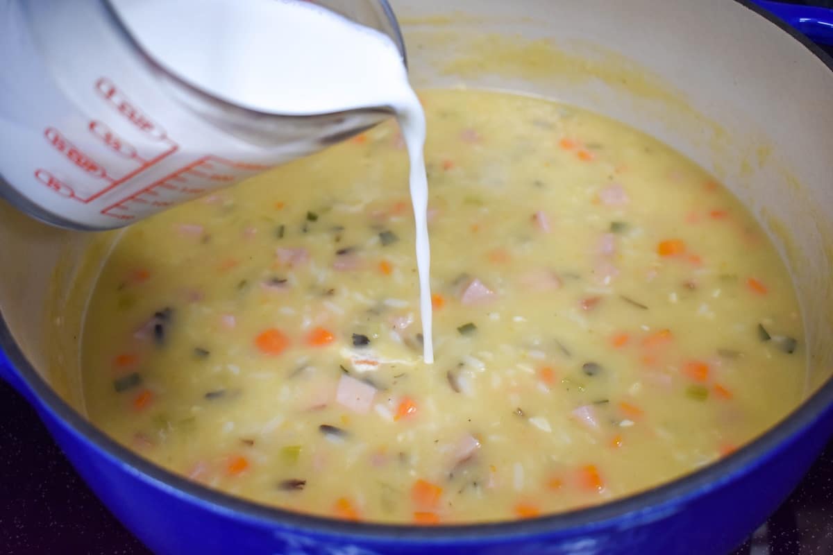 The cream being added to the ham and wild rice soup still in the pot.