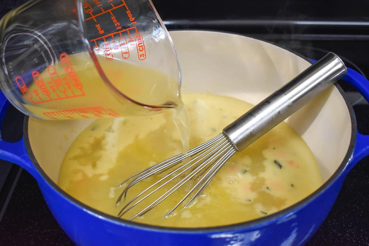 Chicken broth being added to the ingredients in the pot with a whisk is in the pot.