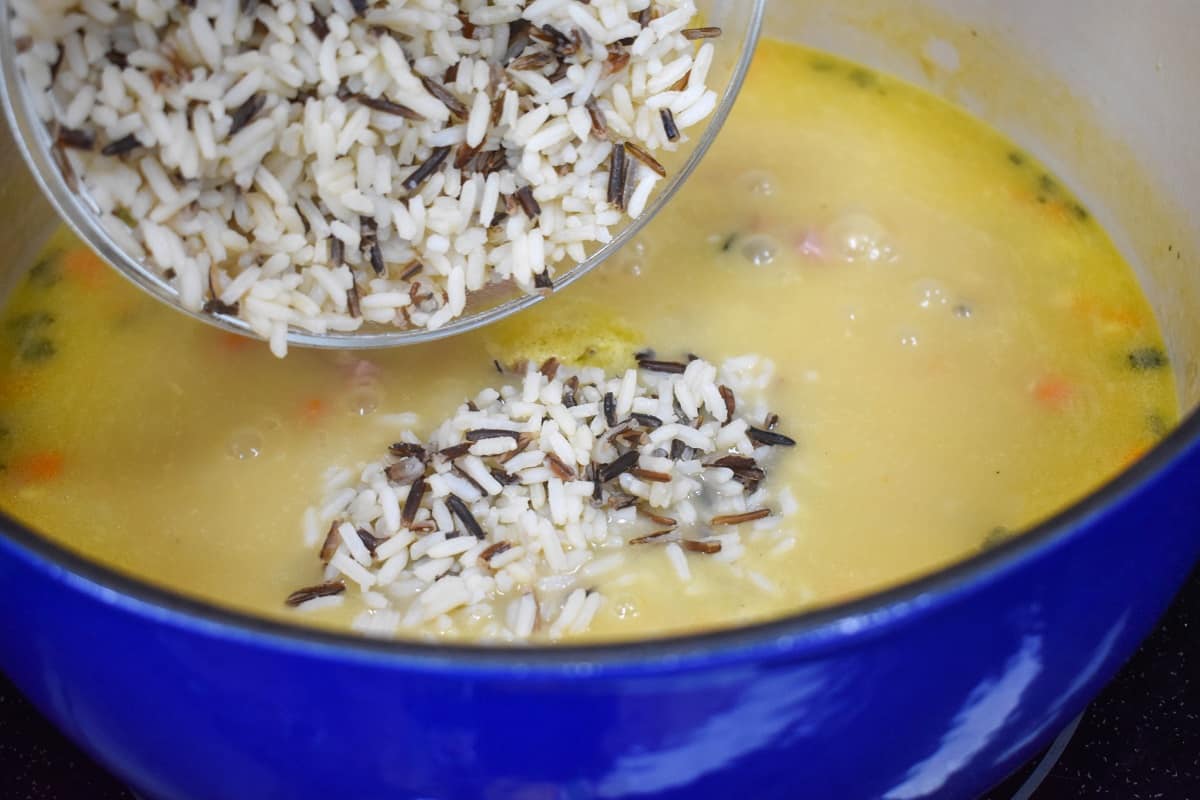 Cooked white and wild rice being added to the soup in the pot.