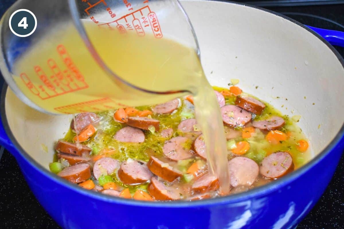 Chicken broth being poured into the pot over the sausage and vegetables.
