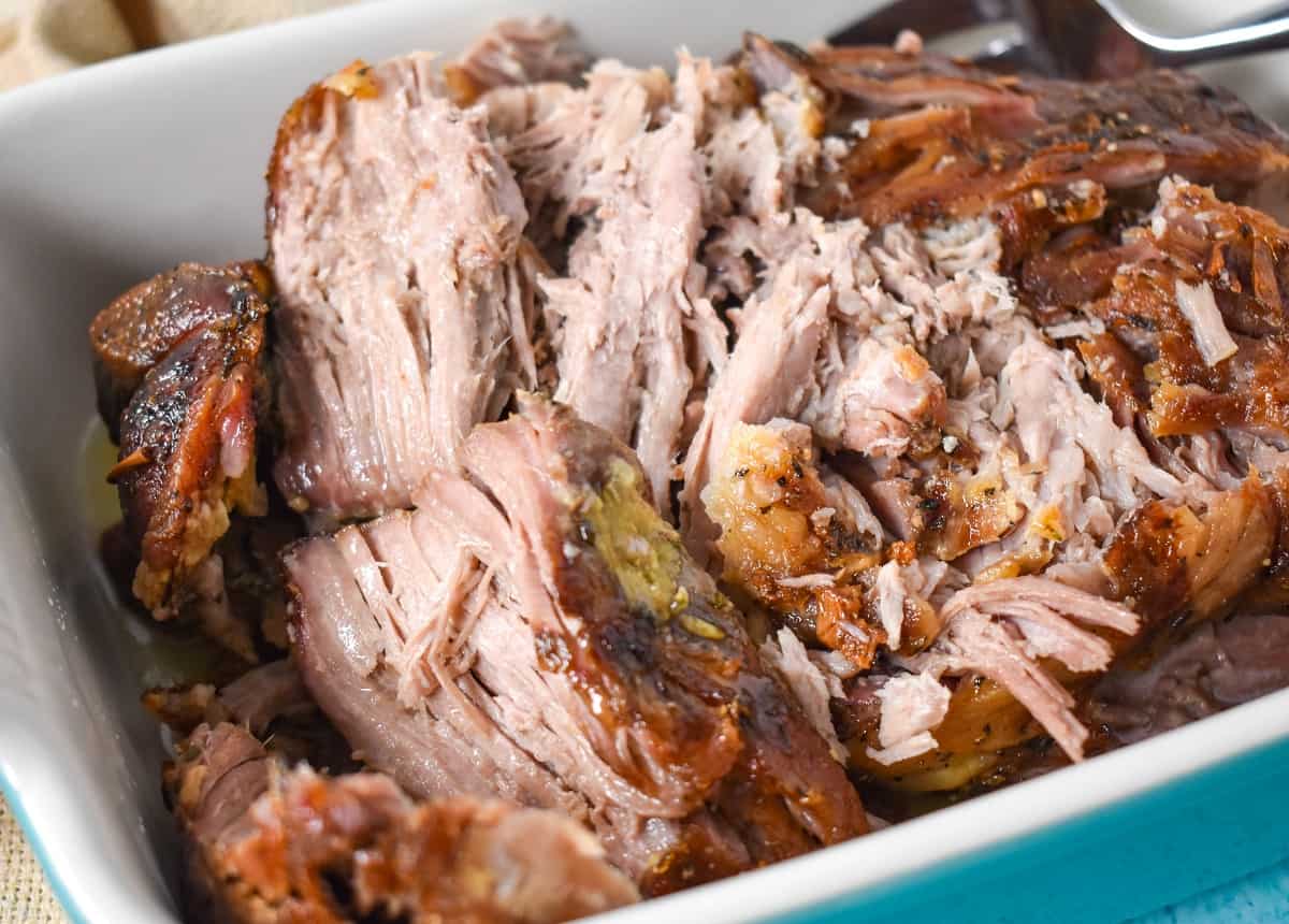 The roasted pork shoulder shredded into large chunks in a white baking dish.