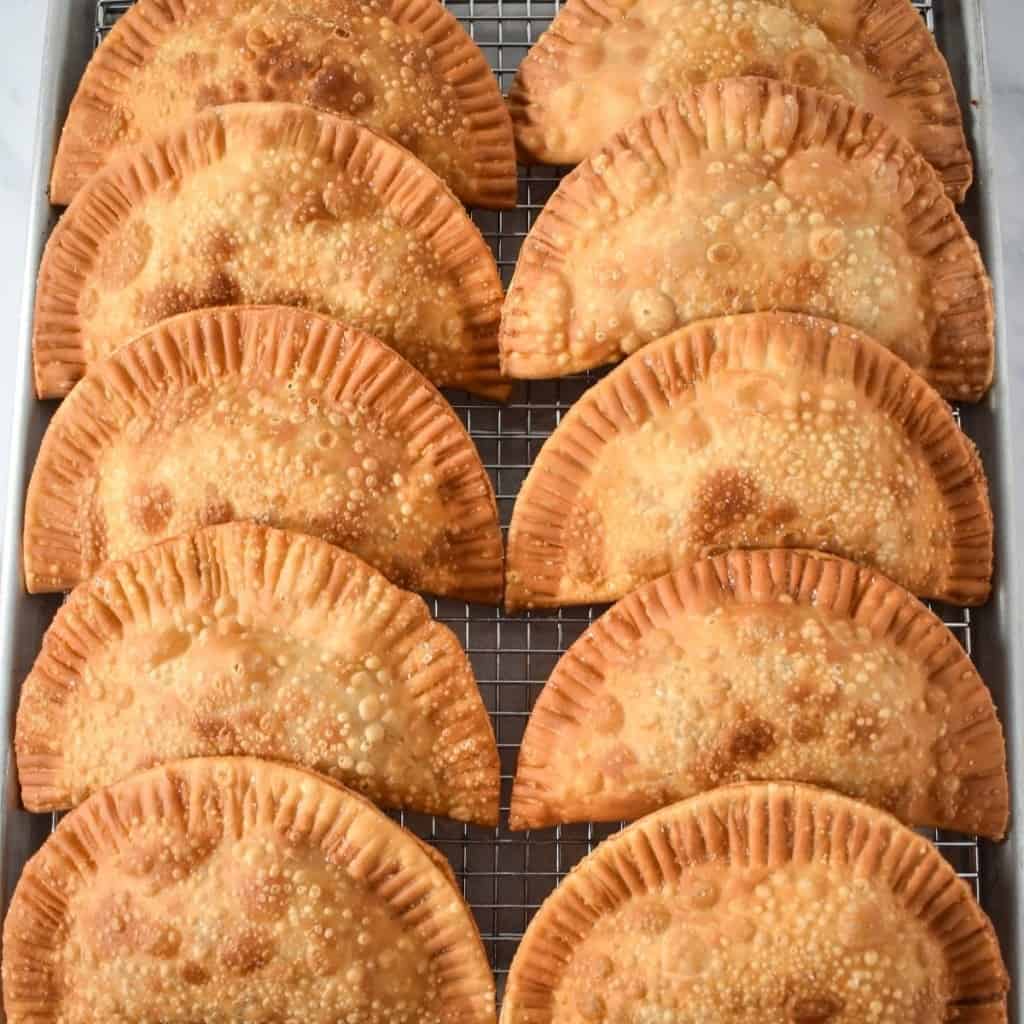 An image of 10 empanadas lined up in two rows on a baking sheet lined with a cooling rack.