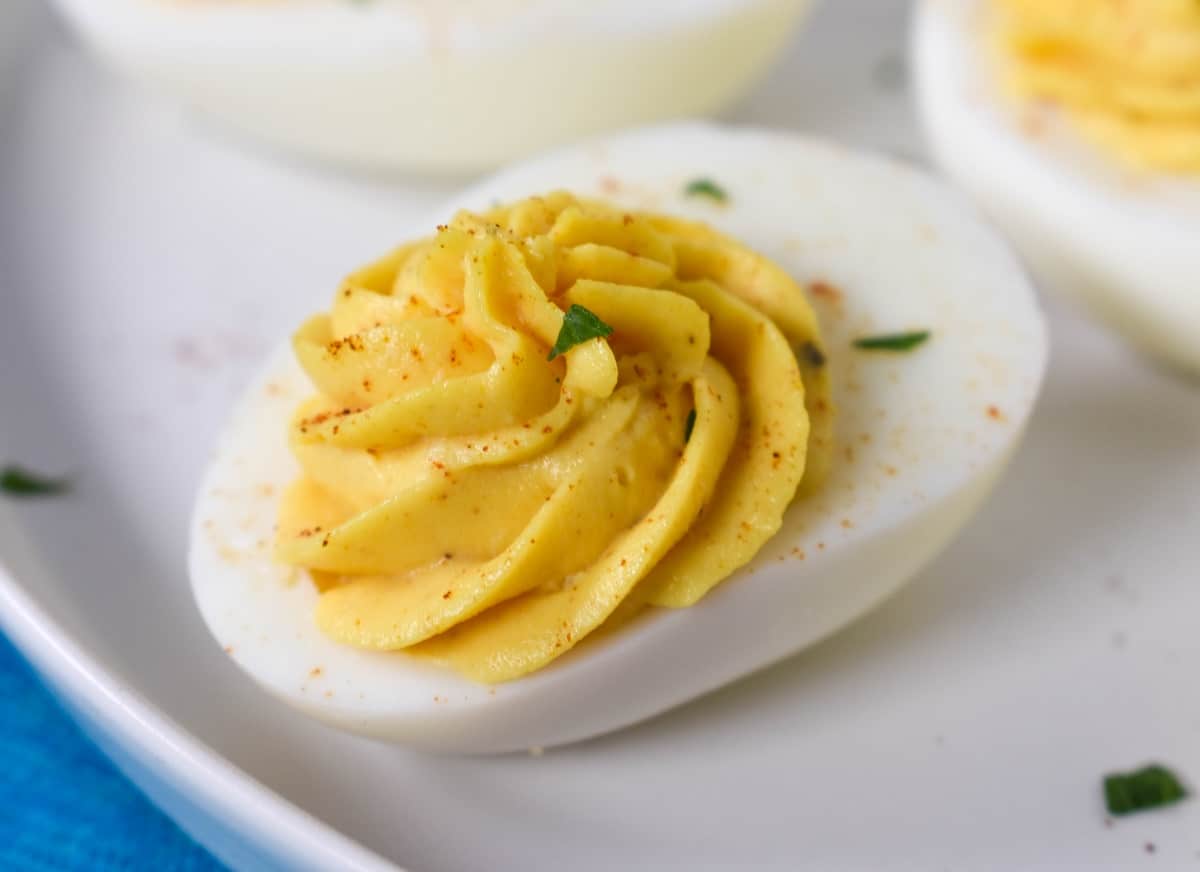 A close up image of one finished deviled egg on a white plate.