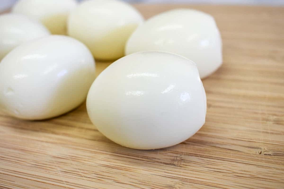 An image of six peeled hard boiled eggs set on a wood cutting board.