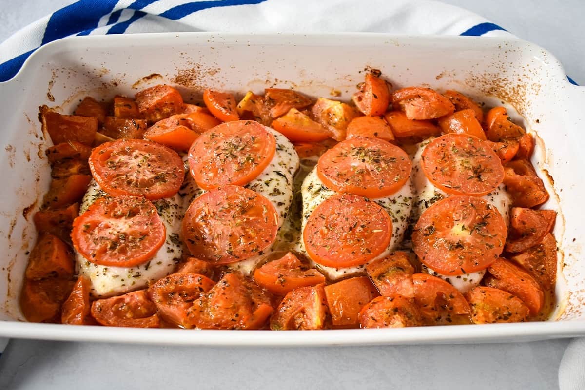 The baked chicken and tomatoes in a white baking dish.