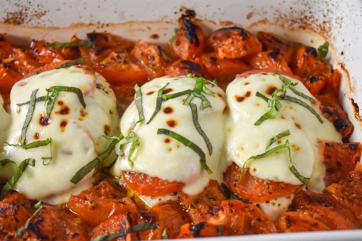 The finished baked chicken caprese garnished with basil and still in the white baking dish.