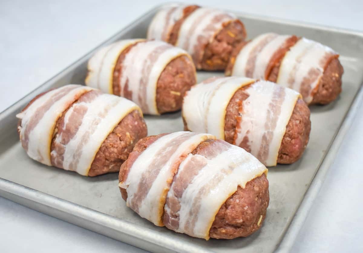 An image of six meatloaves wrapped in bacon and set on a baking sheet.