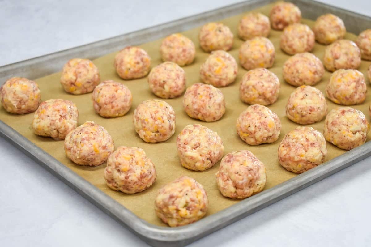 An image of the sausage mixture formed into balls and arranged on a parchment paper lined baking sheet.