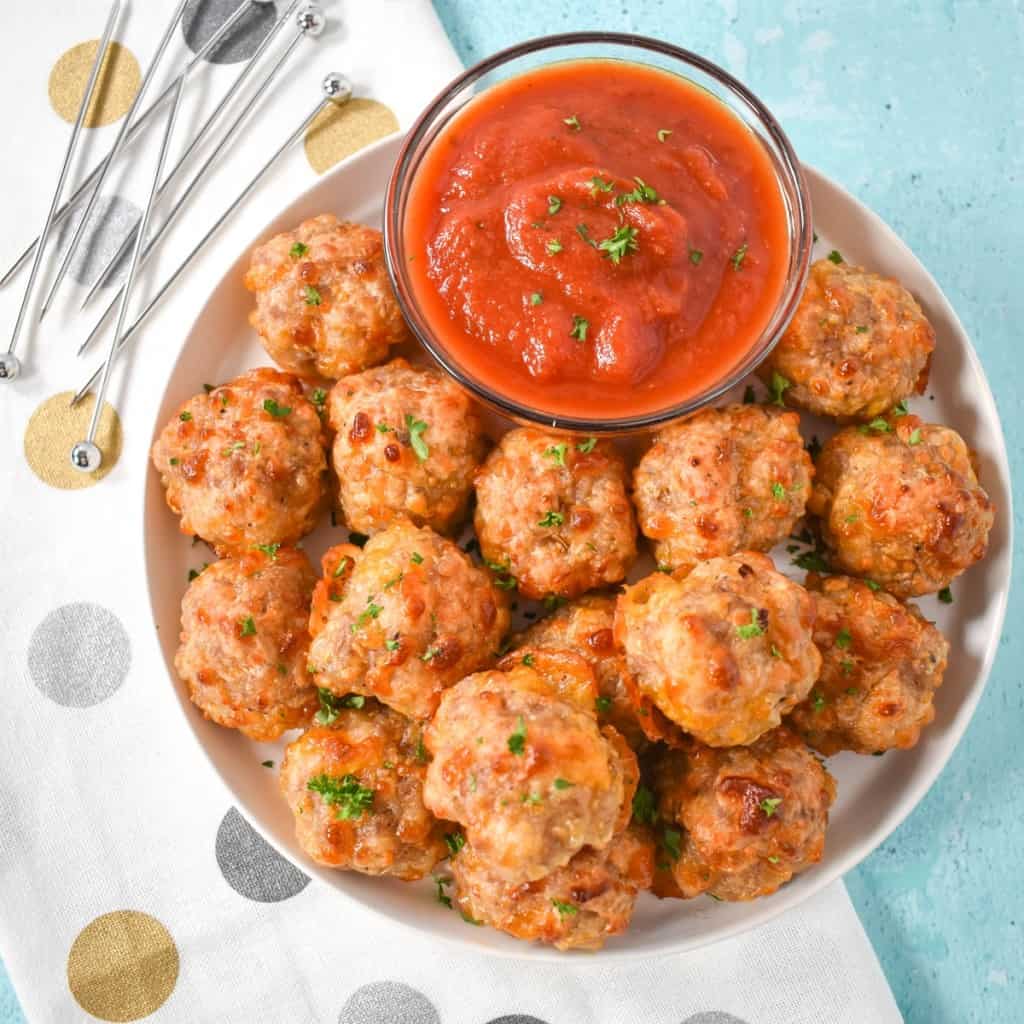The sausage cheese balls arranged on a white plate served with marinara sauce.