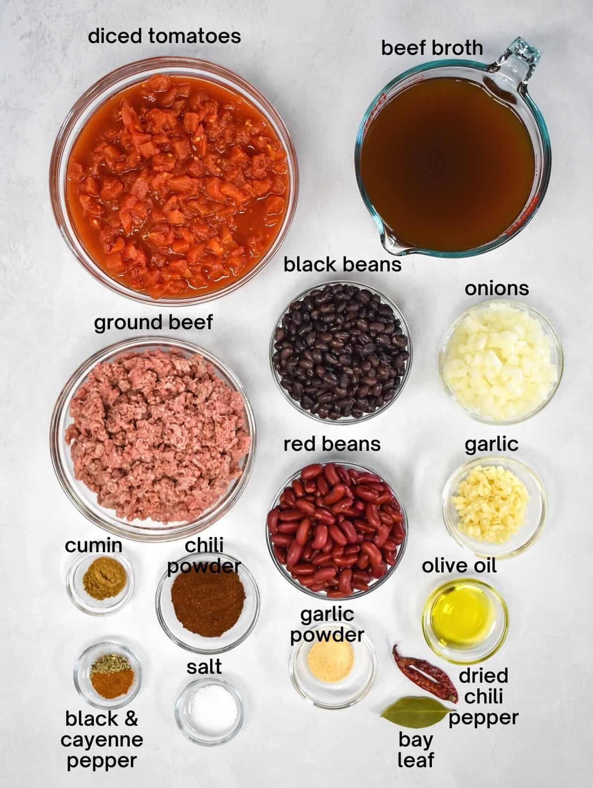 An image of the ingredients for the beef and bean chili arranged in glass bowls on a white table. Each ingredient has a label in small black letters.
