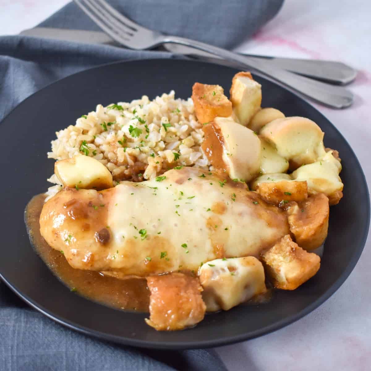 The finished French onion chicken served with brown rice on a black plate.