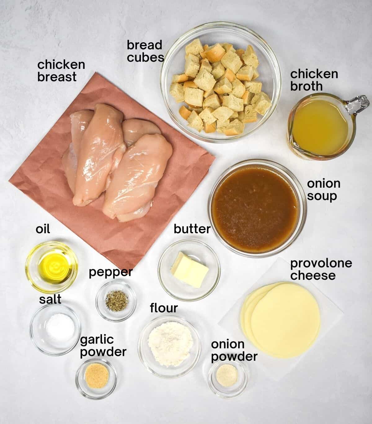 The ingredients for the dish arranged on a white table. Each ingredient is labeled with the name in small, black letters.