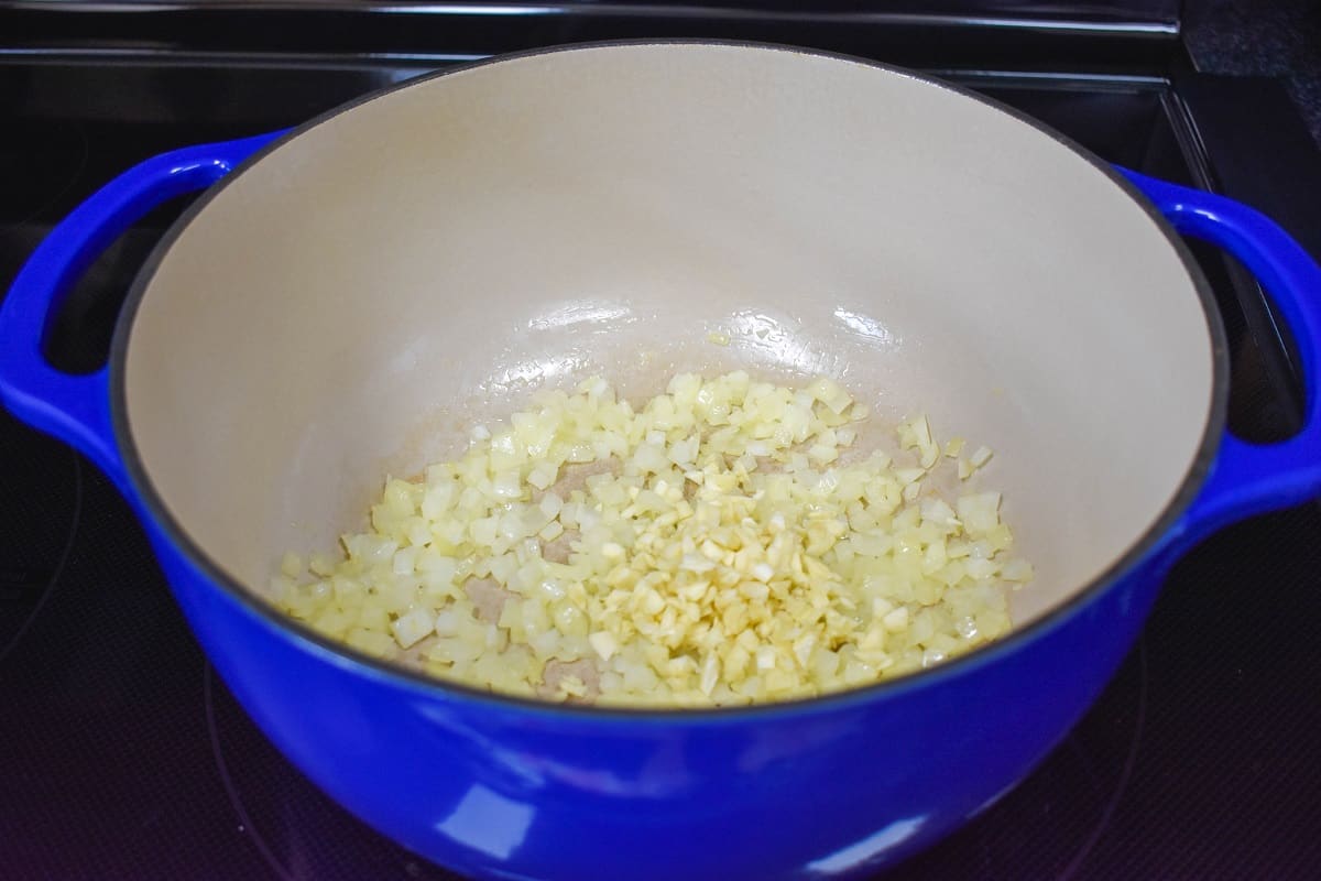 An image of onions and garlic cooking in a large blue pot.