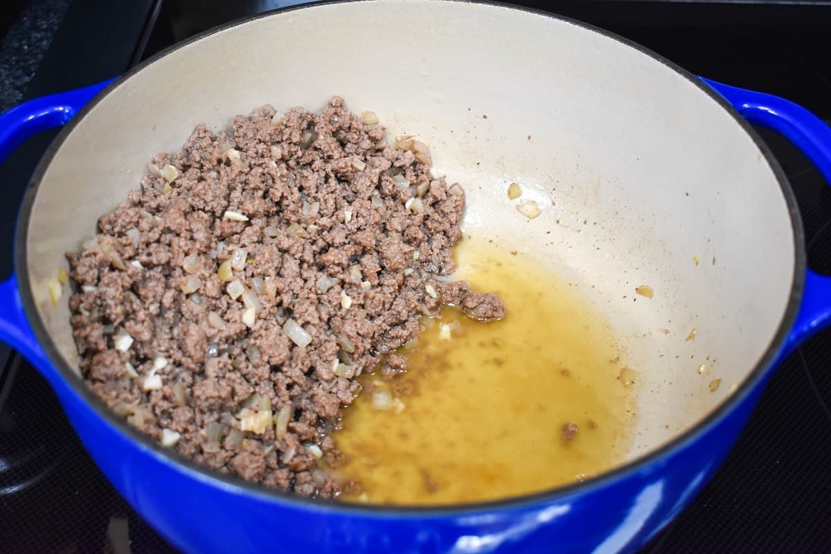 An image of browned ground beef in a large pot that is arranged to one side so the oil is pooled on the other side.