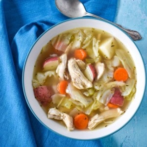 The chicken cabbage soup served in a white bowl with an aqua linen.