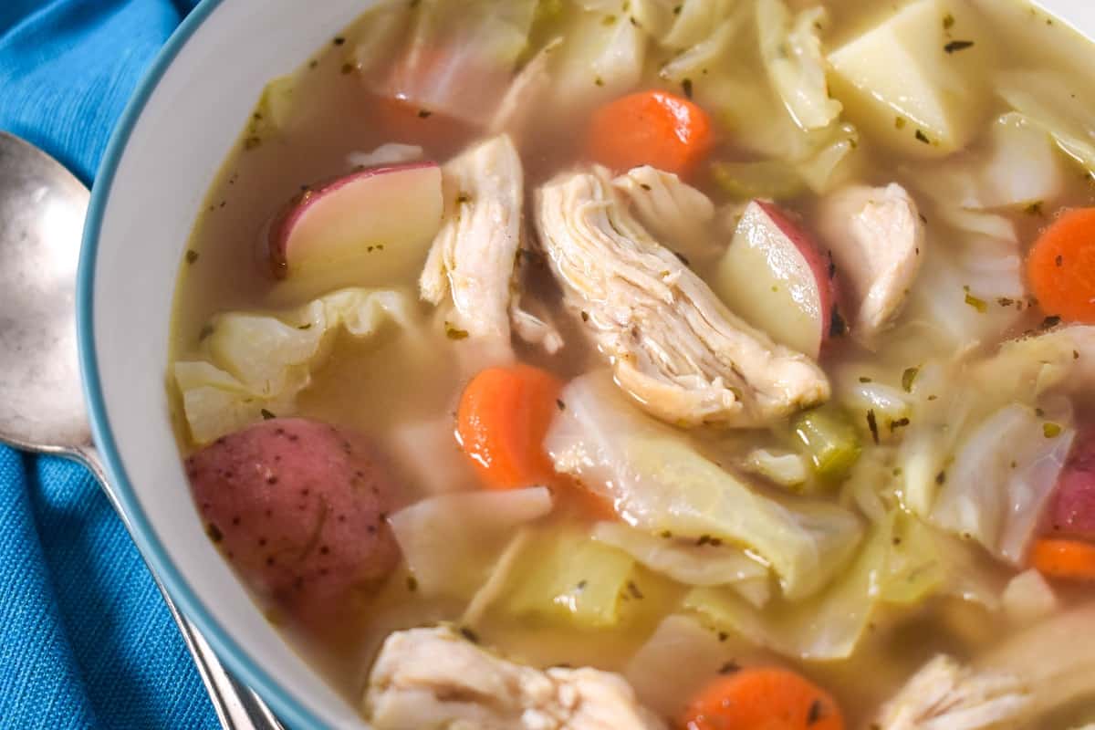 A close up image of the chicken cabbage soup served in a white bowl with an aqua rim.