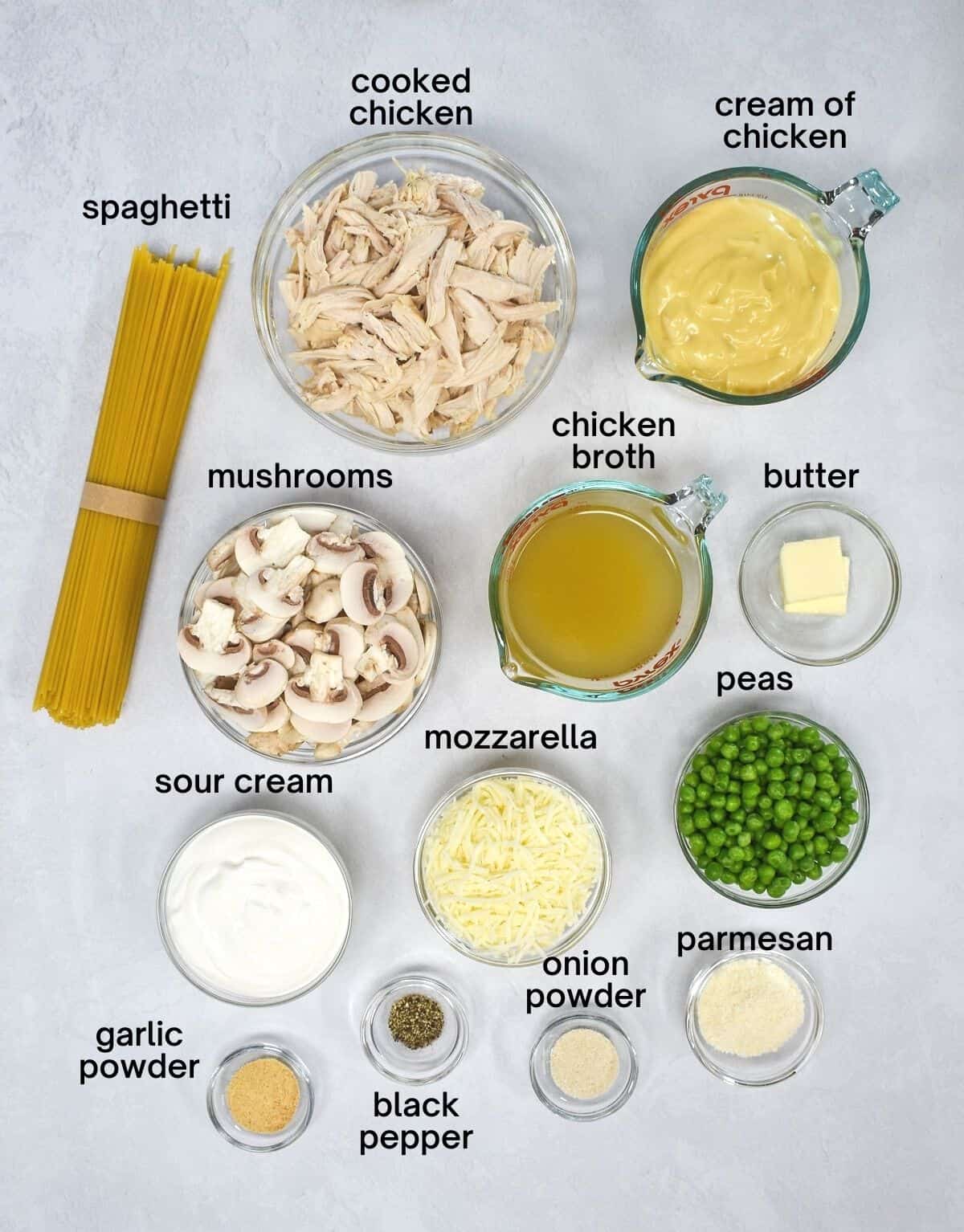 The prepped ingredients for the tetrazzini arranged in glass bowls on a white table. Each ingredient has the name in small black letters.