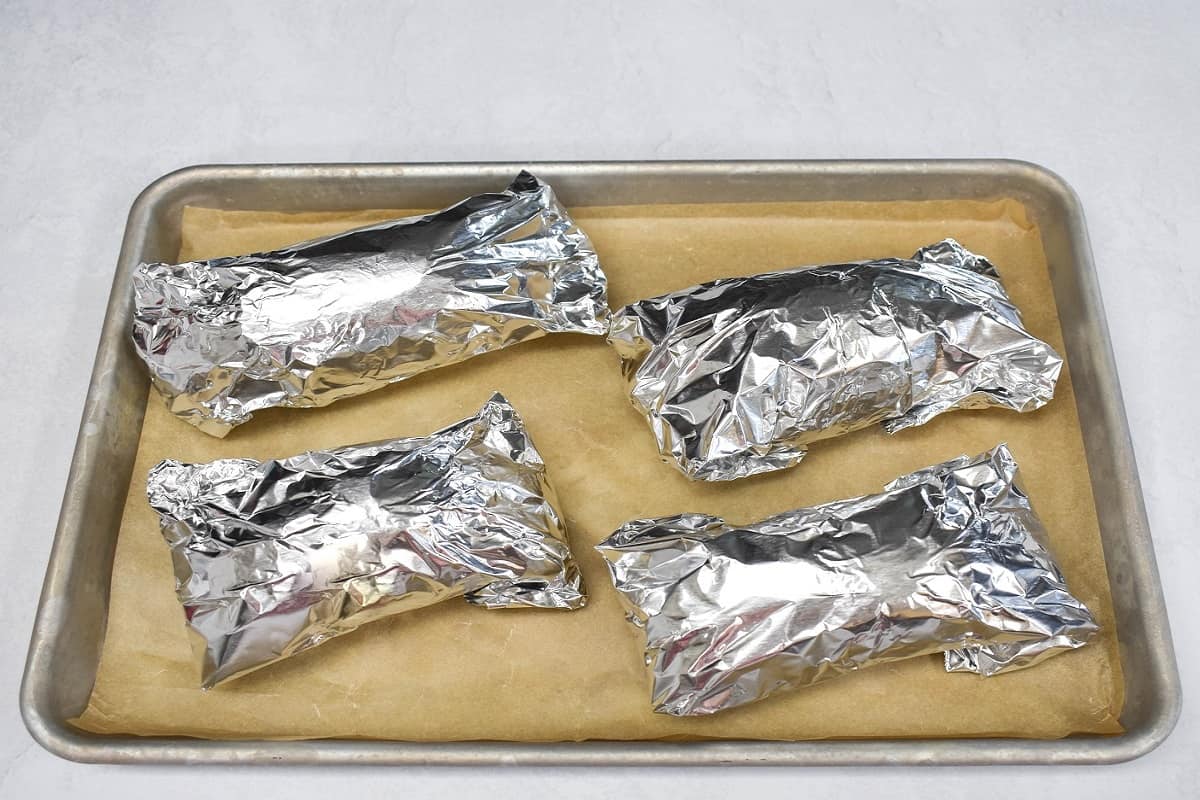 Four sweet potatoes wrapped in foil on a baking sheet lined with parchment paper.