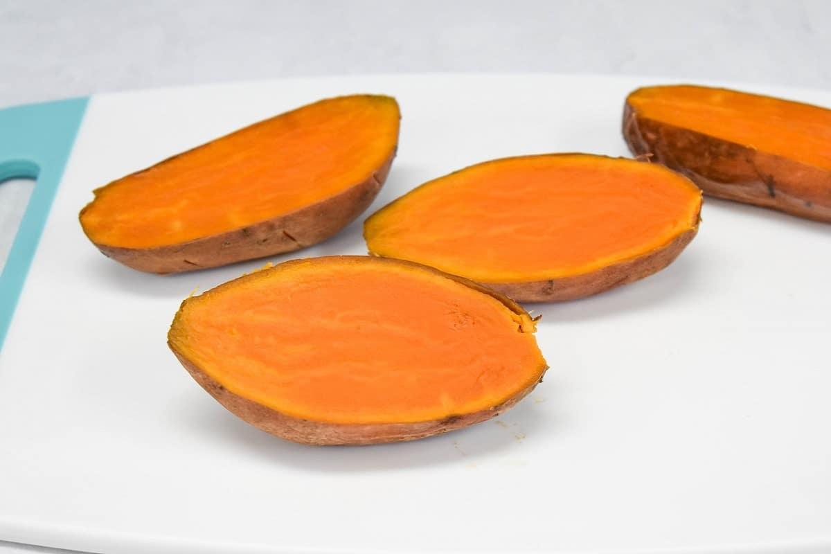 Sweet potatoes cut in half on a white cutting board.