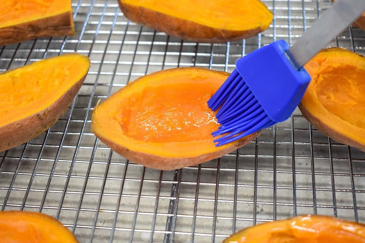 A scooped, halved sweet potato being brushed with oil with a blue silicone brush.