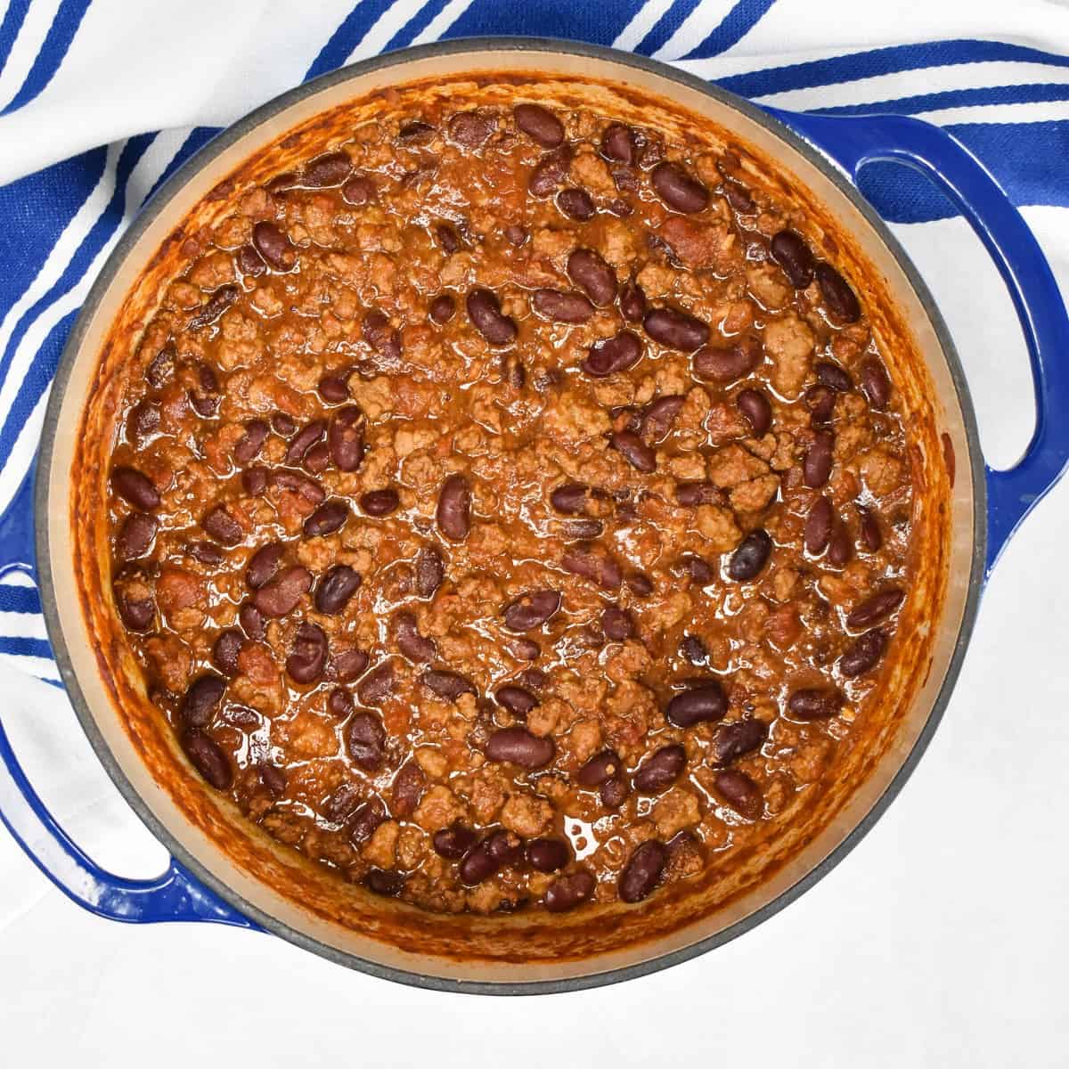 A top shot of the finished chili still in the pot, set on a white table with a blue and white stripe towel.