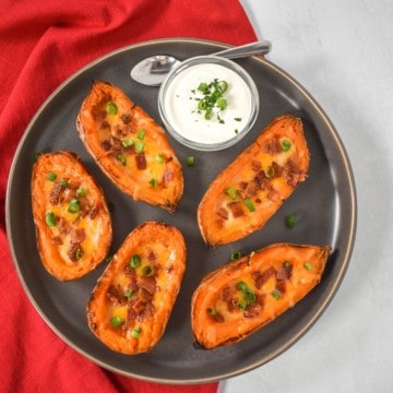 An image of five sweet potato skins arranged on a gray platter, served with a side of sour cream.