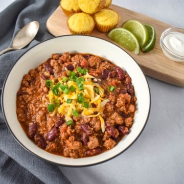 The turkey chili served in a white bowl with a black rim and garnished with shredded cheese and green onions.