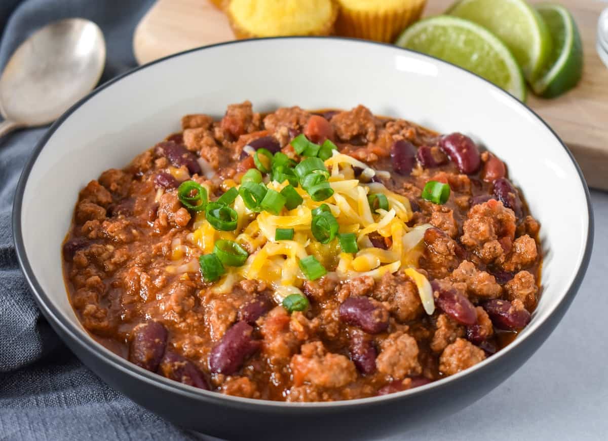 A close up image of the turkey chili served in a white bowl with a black rim and garnished with cheese and green onions.