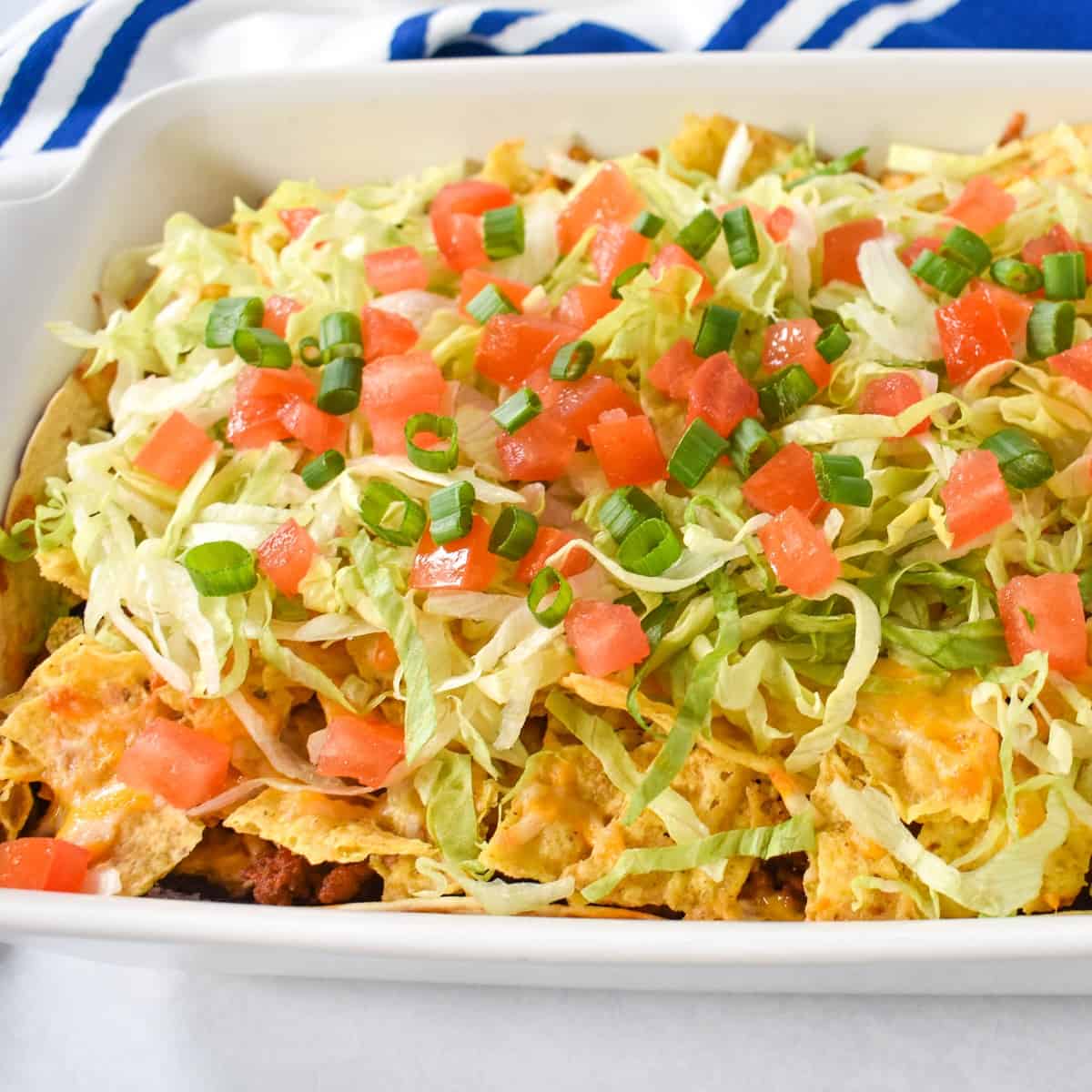 A close up of the finished casserole garnished with shredded lettuce, diced tomatoes, and green onions.