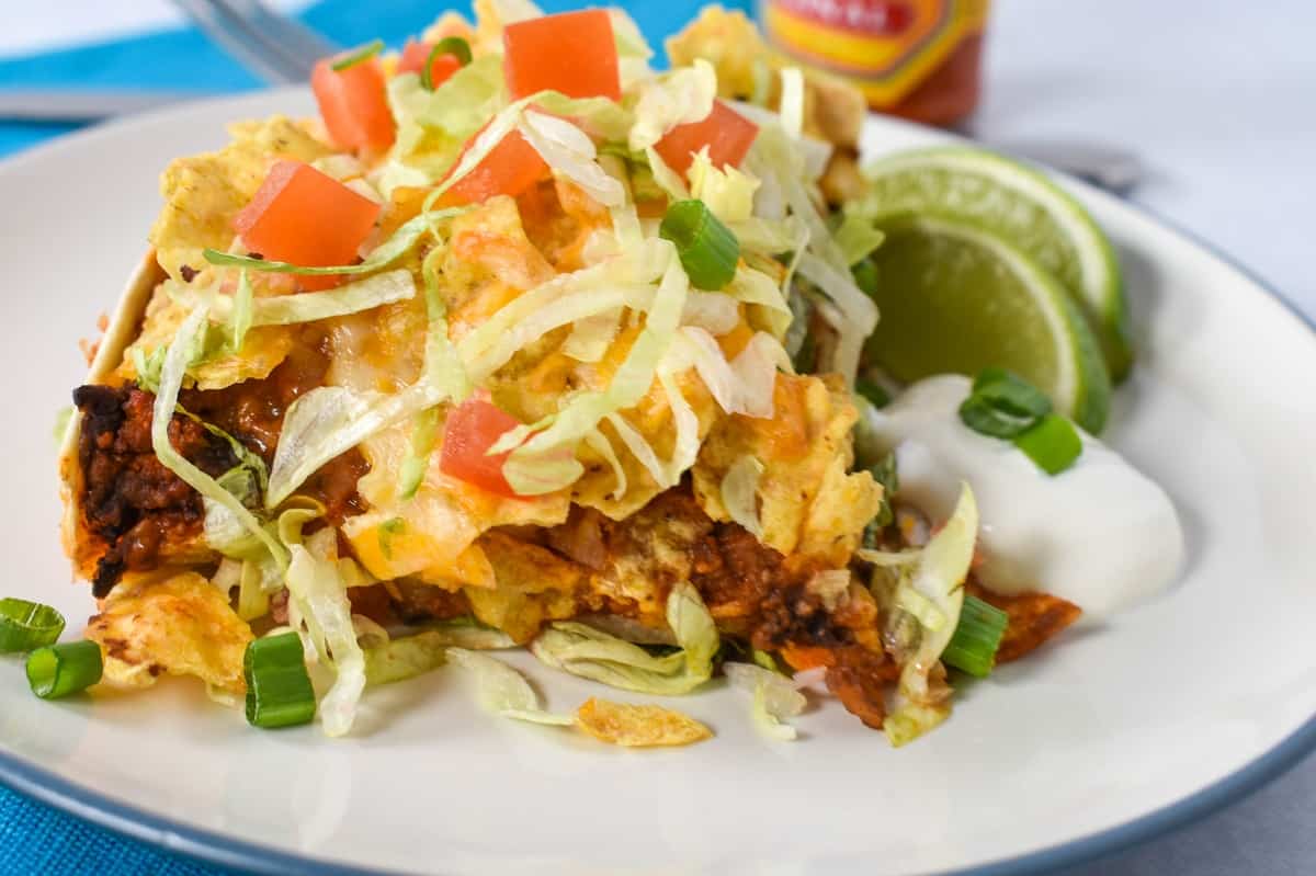 A close up image of the turkey taco casserole served on a white plate with a side of sour cream and lime wedges.
