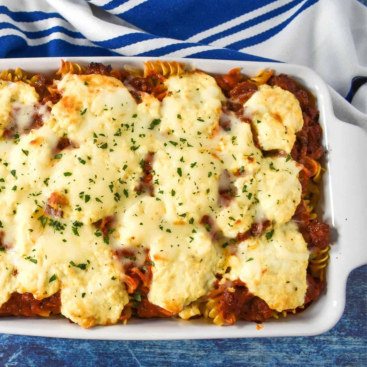 An image of the lasagna casserole in a white baking dish with a blue and white stripe towel.