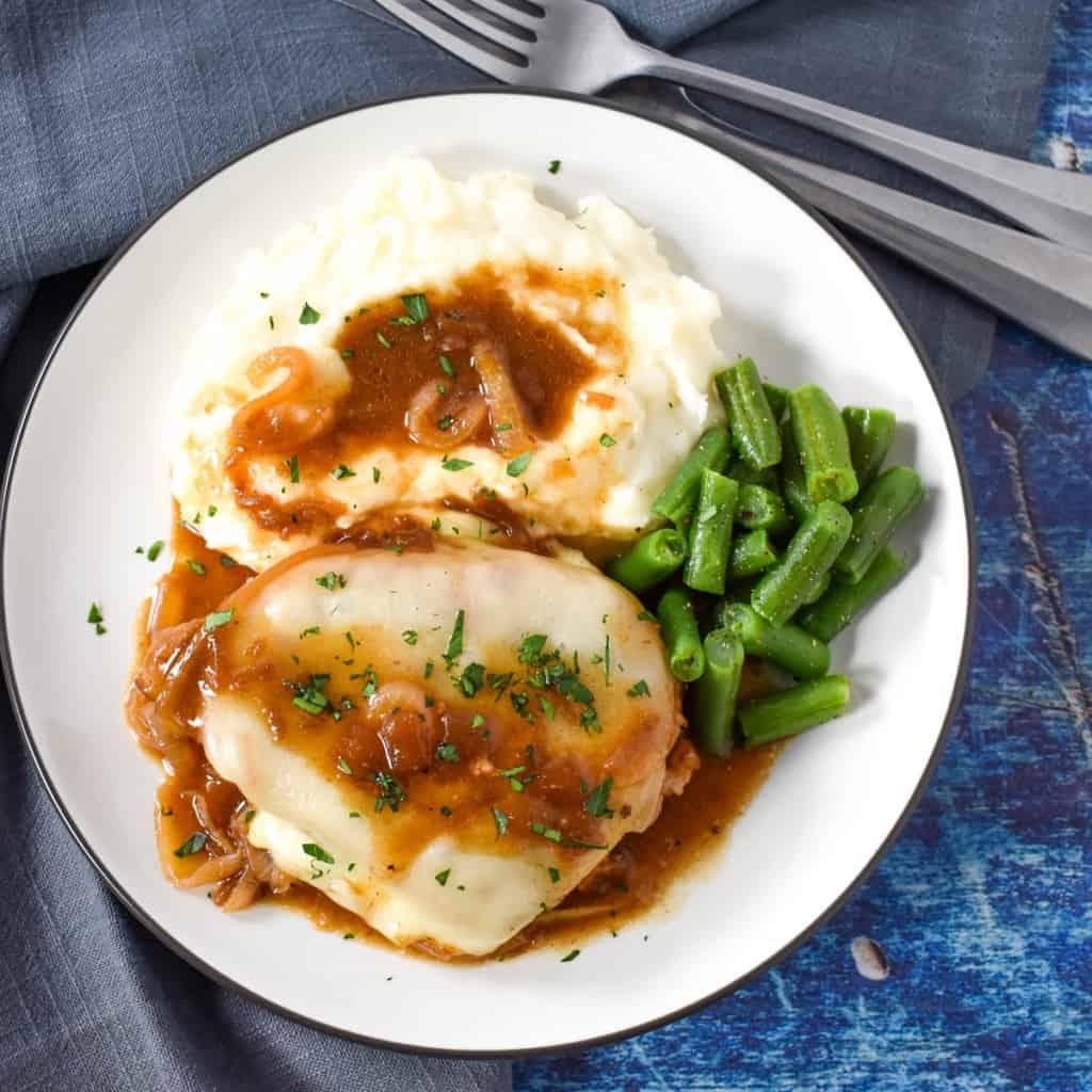 An image of the french onion pork chop served with mashed potatoes, covered with the onion sauce and a side of green beans.