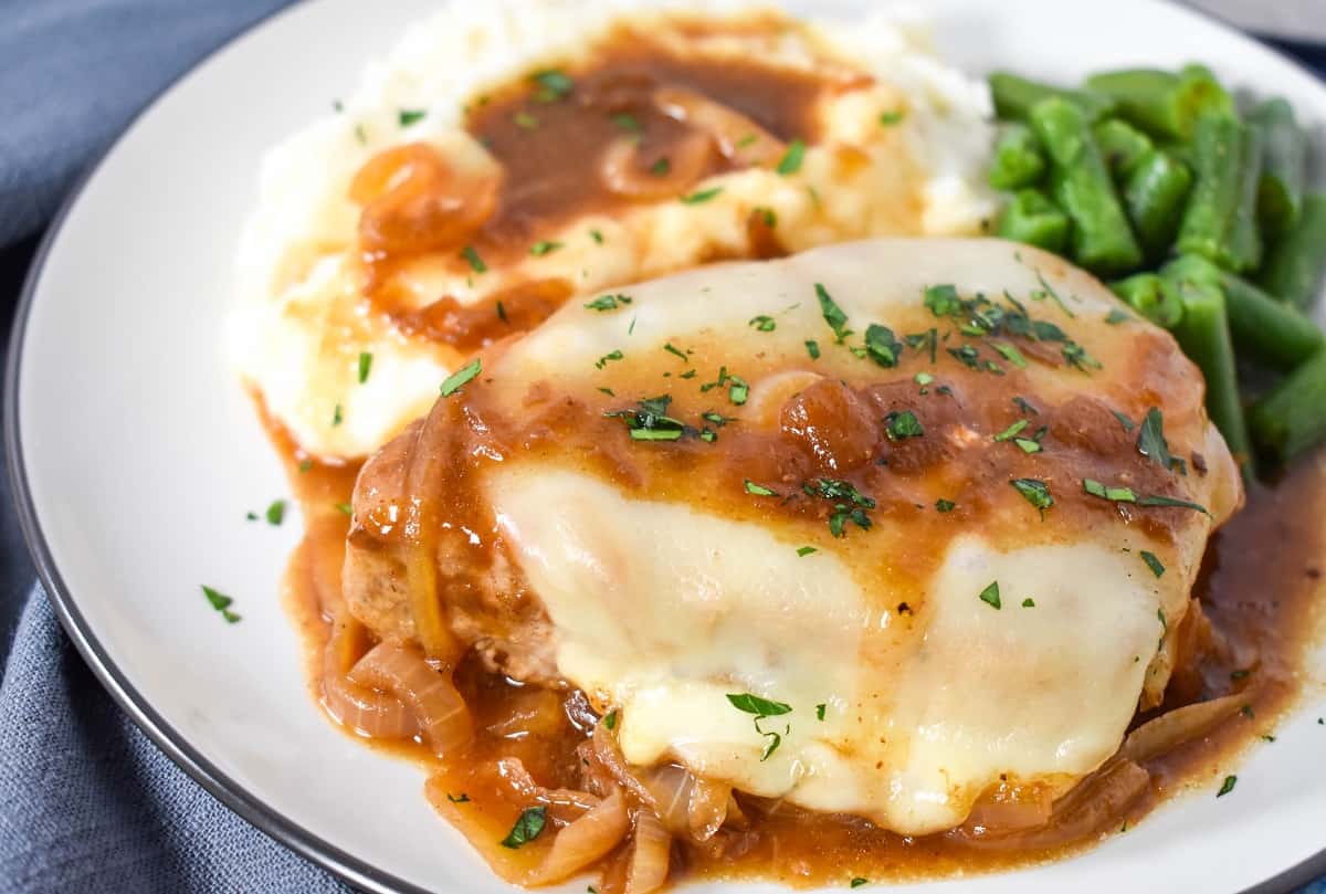 A close-up of the pork chop served with the onion sauce, mashed potatoes and green beans.