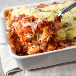 Easy lasagna casserole with layers of rotini, sausage sauce, ricotta, and melted mozzarella being served with a spoon from a white baking dish.