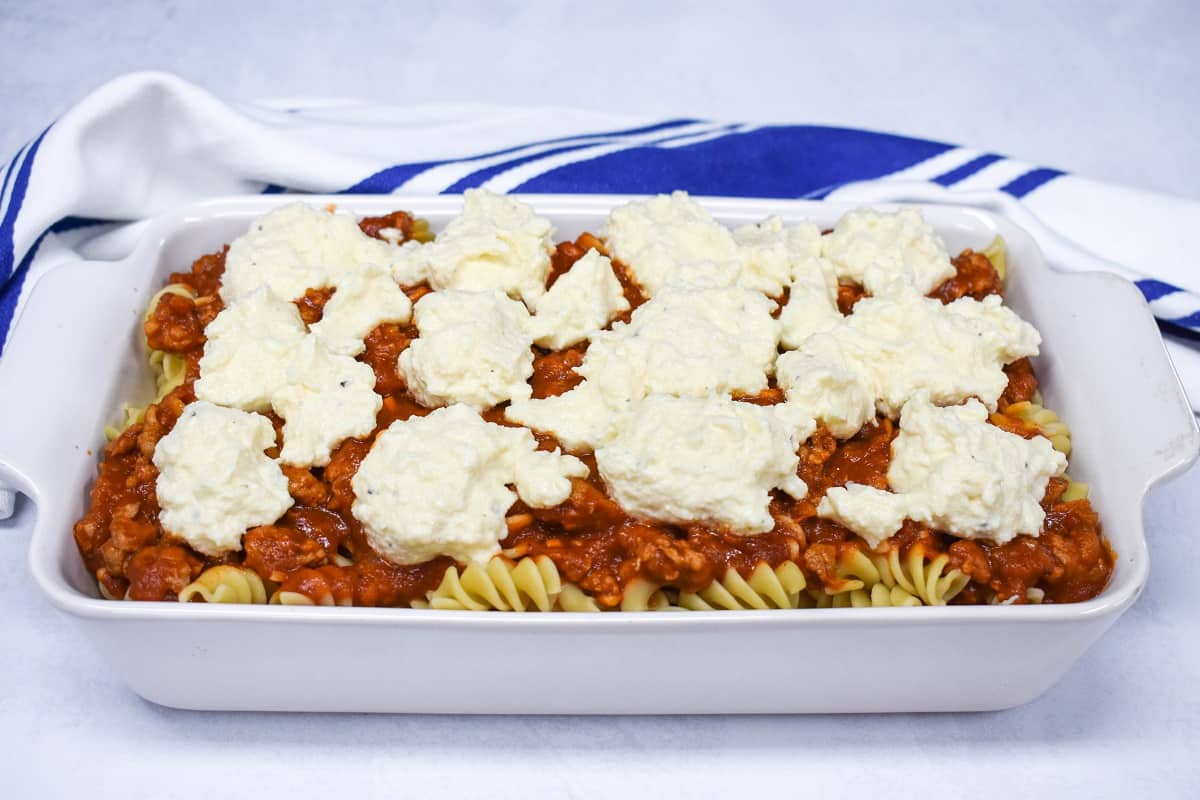 The prepared casserole before baking, set on a white table with a blue and white kitchen towel.