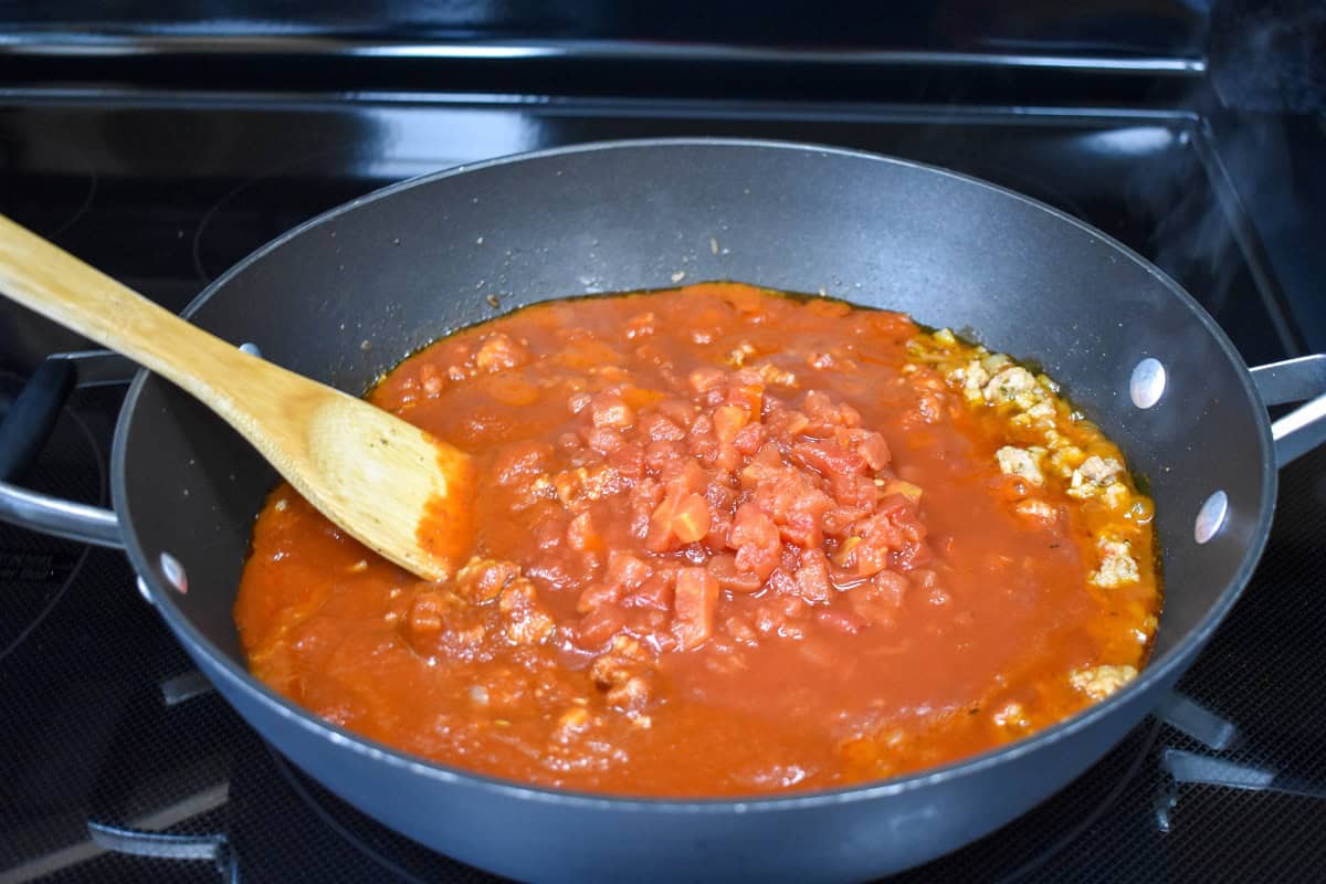 Diced tomatoes and pasta sauce in a skillet with the browned Italian sausage, stirred with a wooden spoon.